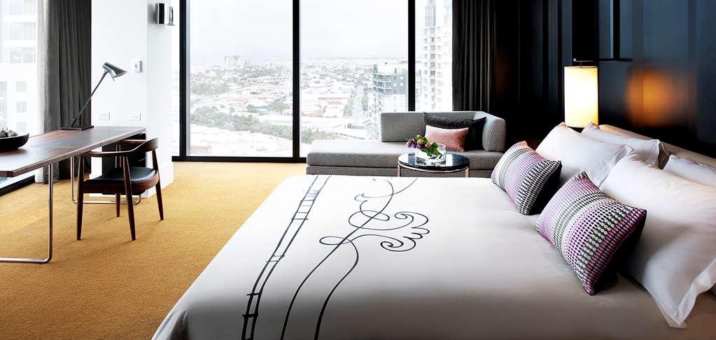 Hotel Crown Metropol Melbourne Camera foto The photo shows a stylish hotel room featuring a large bed with a decorative white bedspread that has a swirling black design. Two decorative pillows are placed at the head of the bed. In the background, there is a sofa with cushions, situated next t