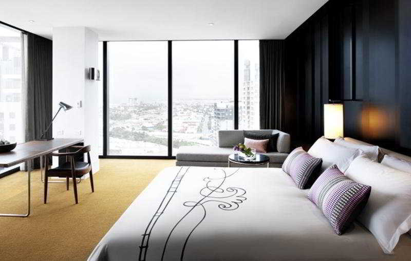 Hotel Crown Metropol Melbourne Esterno foto The photo depicts a modern hotel room that features a stylish and contemporary design. 

- **Bed**: There is a large bed with decorative pillows and an elegantly designed bedspread.
- **Seating Area**: Next to the bed is a gray sofa that complements 