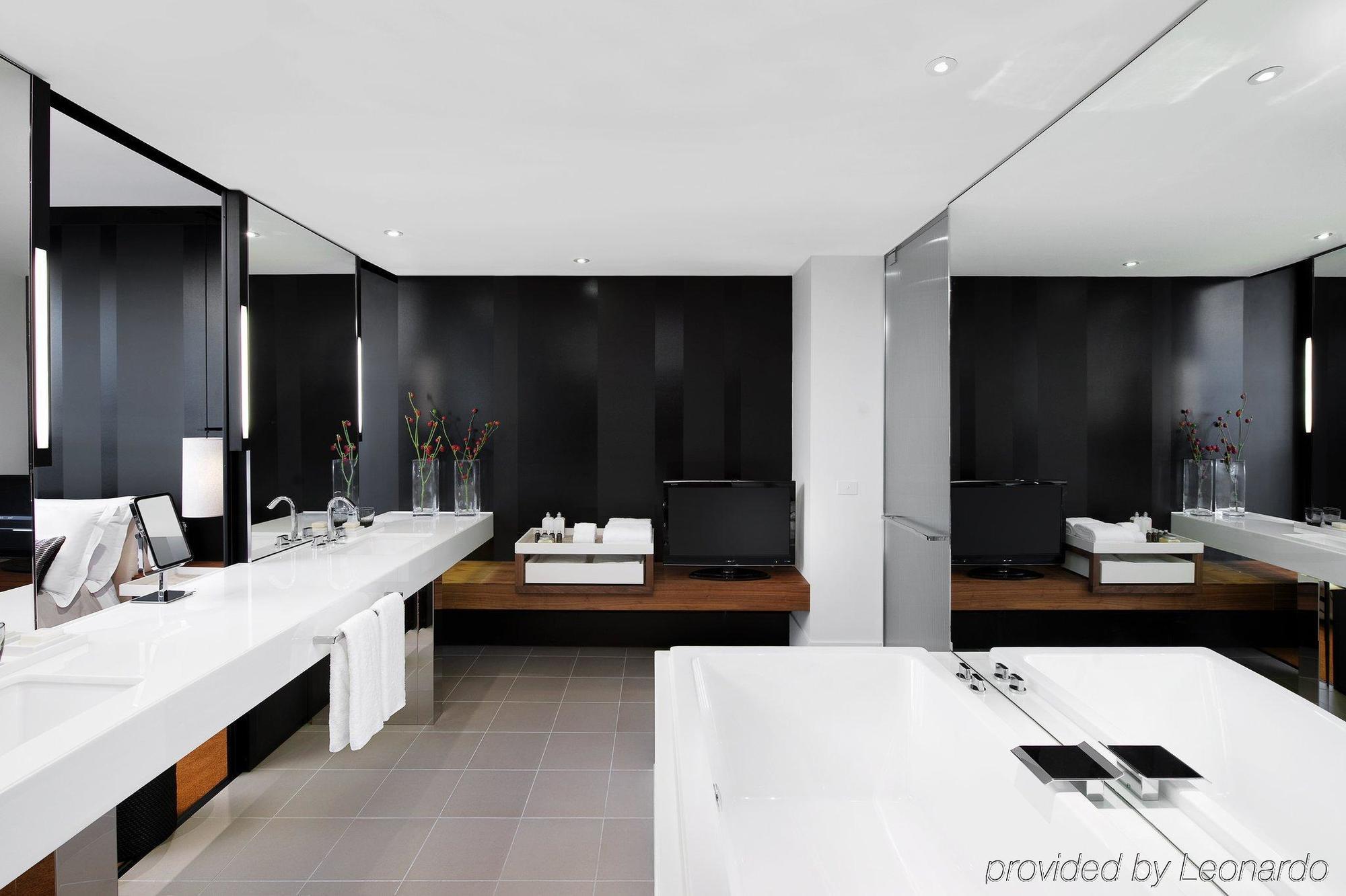 Hotel Crown Metropol Melbourne Servizi foto The photo shows a modern bathroom designed with a sleek and minimalist aesthetic. It features a long, white countertop basin with integrated sinks, surrounded by dark walls and large mirrors that enhance the space's brightness. In the center, there i