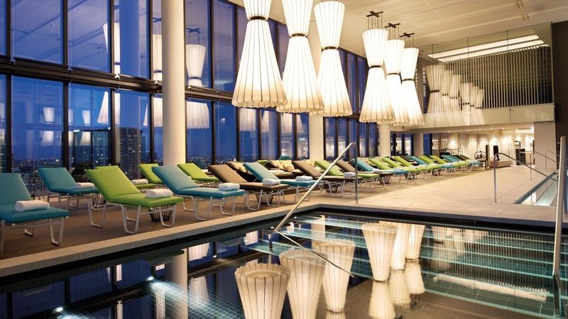 Hotel Crown Metropol Melbourne Esterno foto The photo shows a modern, stylish indoor pool area with large windows that provide a view of the city. The room is beautifully lit by distinctive, large pendant lights that hang from the ceiling. Alongside the pool, there are several lounge chairs in