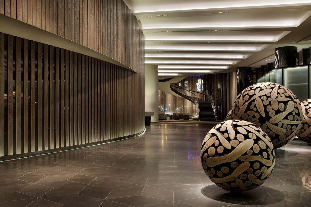 Hotel Crown Metropol Melbourne Esterno foto The photo shows a modern and stylish interior space, likely of a hotel lobby or a public area. The design features a curved wall made of wood, creating a warm ambiance. The flooring appears to be dark stone tiles, contributing to the contemporary loo