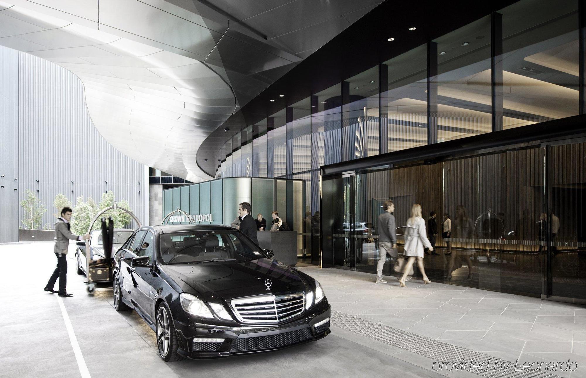 Hotel Crown Metropol Melbourne Esterno foto The image depicts a modern urban setting with a sleek, black luxury sedan parked in front of a sophisticated building. The architecture features clean lines and a combination of glass and metallic elements. In front of the entrance, there are people 