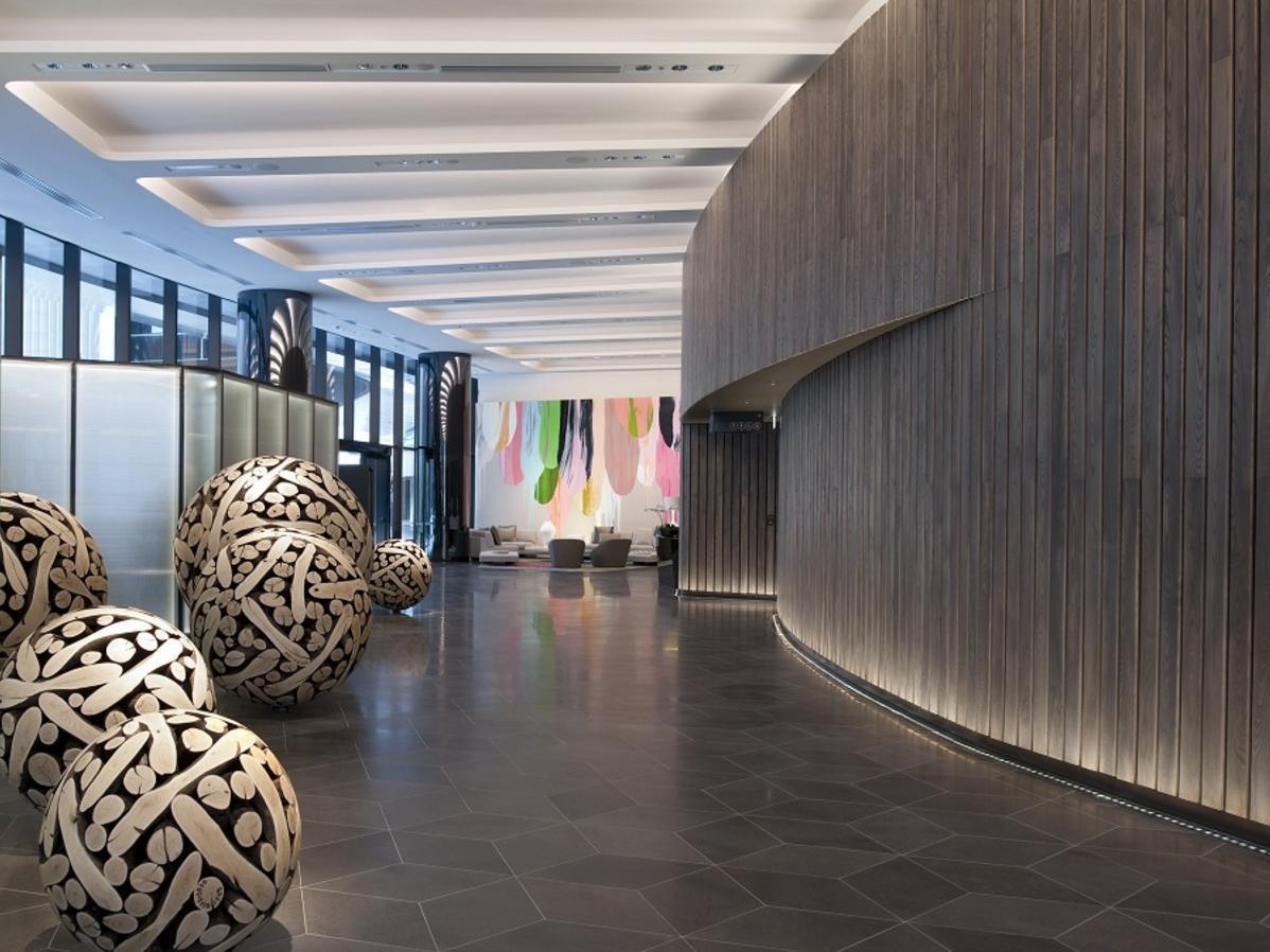 Hotel Crown Metropol Melbourne Esterno foto The photo shows a modern indoor space, likely a lobby or reception area. It features a smooth, curved wooden wall and a polished dark floor. Large, decorative spheres with intricate black and white patterns are positioned in the foreground, adding a 
