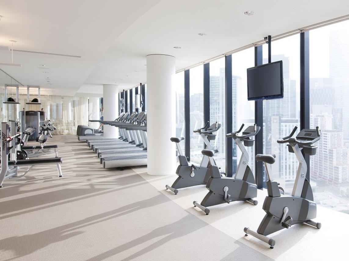 Hotel Crown Metropol Melbourne Esterno foto The photo shows a modern gym with large windows offering a panoramic view of the city outside. The gym features several pieces of exercise equipment, including stationary bicycles and treadmill machines. There are also benches for workouts visible in