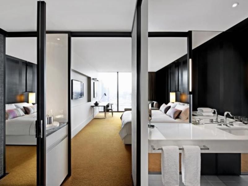 Hotel Crown Metropol Melbourne Esterno foto The photo shows a modern hotel room with a stylish and sleek design. The space is divided by glass and panel partitions, creating a sense of openness. 

On one side, there is a large bed with soft linens and decorative pillows, accompanied by bedside