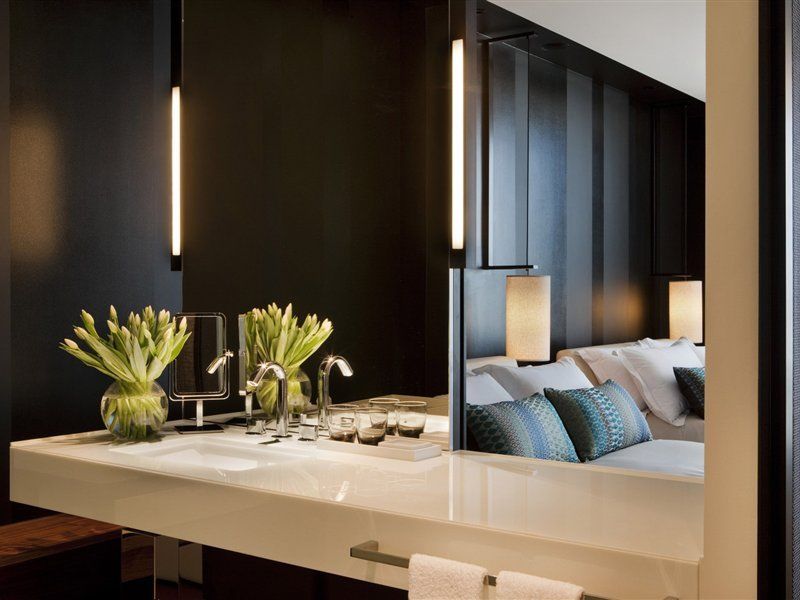Hotel Crown Metropol Melbourne Esterno foto The photo shows a modern interior space that appears to be a blend of a bathroom and a living area. In the foreground, there's a sleek, white countertop with a sink and faucets. Two vases of fresh, vibrant flowers are positioned on one side. In the b