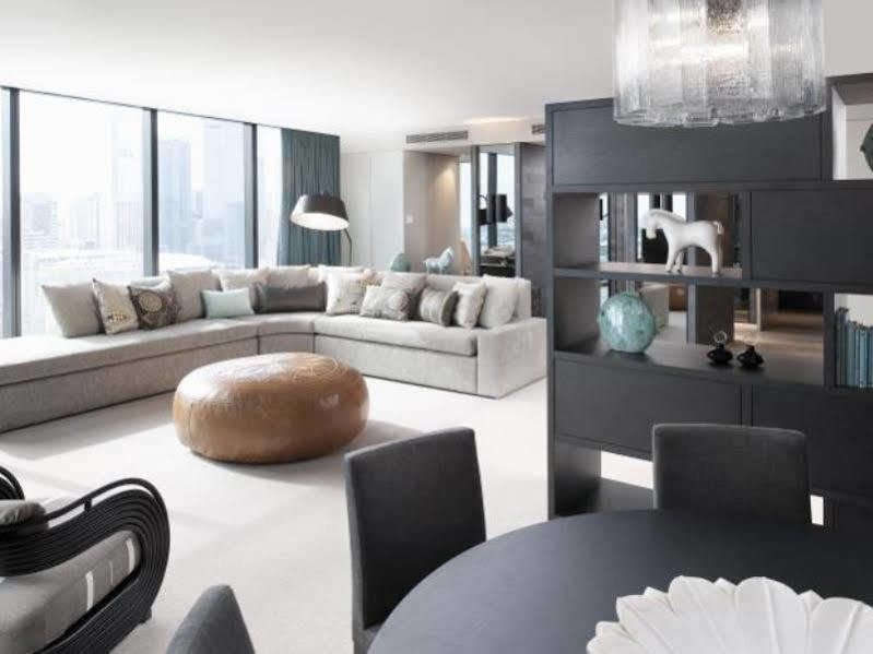 Hotel Crown Metropol Melbourne Esterno foto The photo shows a modern and stylish living space. There is a spacious living area featuring a large, light-colored sectional sofa with plenty of cushions. In the center, there is a rounded, metallic coffee table. To one side, there is a black booksh