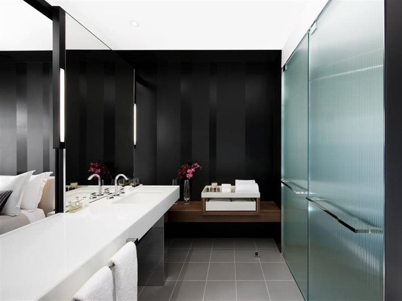 Hotel Crown Metropol Melbourne Esterno foto The photo shows a modern bathroom with a sleek and minimalist design. The walls are painted in a dark color, creating a sophisticated ambiance. There is a long, white countertop with two sinks, alongside modern faucets. Below the countertop, there ar