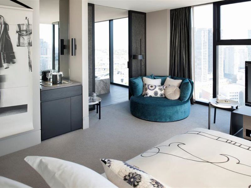Hotel Crown Metropol Melbourne Esterno foto The photo depicts a modern hotel room featuring stylish and contemporary decor. In the foreground, there is a bed with a patterned coverlet. Next to the bed, there is a small table or nightstand. 

The room has large windows that let in plenty of nat